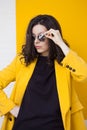 Stylish and daring young brunette in a bright yellow jacket and mirrored sunglasses.