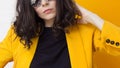 Stylish and daring young brunette in a bright yellow jacket and mirrored sunglasses.