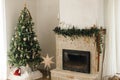 Stylish decorated fireplace mantel with christmas branches, decorations and bells on background of modern christmas tree with