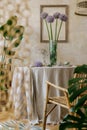 Stylish dining room interior with wooden table, design chairs, rattan pendant lamp, spring flowers in vase, beautiful plates. Royalty Free Stock Photo