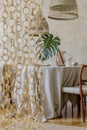 Stylish dining room interior with wooden table, design chairs, rattan pendant lamp, tropical leaf in vase, beautiful plates. Royalty Free Stock Photo