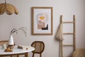 The stylish dining room with round table, rattan chair, wooden commode, pock up poster and kitchen accessories. Beige wall with