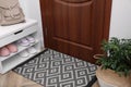 Stylish door mat, houseplant and storage with shoes in hall Royalty Free Stock Photo