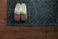 Stylish door mat and slippers on wooden floor, top view. Space for text Royalty Free Stock Photo