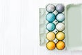 Stylish Easter eggs in carton tray on white wooden background, space for text. Modern colorful easter eggs painted with pastel