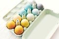 Stylish Easter eggs in carton tray on white wooden background, space for text. Modern colorful easter eggs painted with pastel
