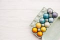 Stylish easter eggs in carton tray on white wooden background, top view. Modern colorful easter eggs painted with natural dye in Royalty Free Stock Photo