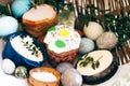 Stylish Easter eggs, easter bread cake, ham, beets, sausage, butter, green branches in wicker basket on white wooden background Royalty Free Stock Photo