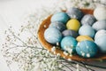 Stylish easter eggs with spring flowers on wooden plate on white wooden background. Modern easter eggs painted with natural dye in Royalty Free Stock Photo