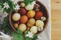 Stylish easter eggs in wooden bowl on rustic table with bunny and spring blooming flowers. Top view