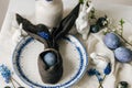 Stylish easter table setting. Easter egg in bunny napkin on vintage plate and spring flowers on rustic table. Happy Easter!