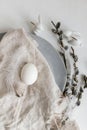 Stylish Easter table setting. Natural easter egg, pussy willow branches, feathers on modern plate with napkin on white wooden