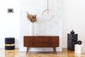 Stylish and eclectic interior of living room with design retro cabinet, round pendant lamp, marble cubes and elegant accessories.