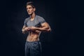 Stylish ectomorph bodybuilder with stylish hair takes off his shirt on the dark background.