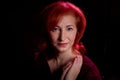 Stylish elderly woman with red hair in vinous dress posing in studio with dark background and red flash and light