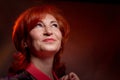 Stylish elderly woman with red hair in vinous dress posing in studio with dark background and red flash and light