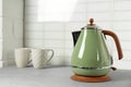Stylish electric kettle and tea cups on grey against white wall