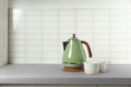 Stylish electric kettle and tea cups on table against white wall, space for text