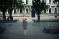 A stylish elegant girl in a dark dress with blond hair stands beautifully in a park alley on a city street Royalty Free Stock Photo