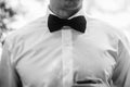 stylish elegant groom tying classic bowtie and smiling in the sunny woods