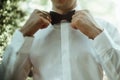 Stylish elegant groom tying classic bowtie and smiling in the sunny woods
