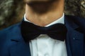 Stylish elegant happy groom in fashionable suit with classic bowtie on background of rocks in mountains