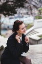 Stylish elegant happy woman sitting on the bench. She dressed in dark coat and sunglasses Royalty Free Stock Photo