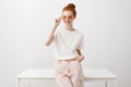 Stylish european ginger girl in trendy sunglasses standing and leaning on table, holding hand in pocket and gazing Royalty Free Stock Photo