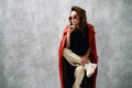 Stylish fashion woman in red coat and trendy casual outfit posing on grey background