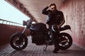 Stylish fashionable biker dressed in a black leather jacket with sunglasses fix the hair and holds helmet while sitting Royalty Free Stock Photo