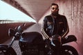 Stylish fashionable biker dressed in a black leather jacket with sunglasses holds a helmet sitting on his custom-made Royalty Free Stock Photo