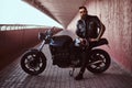 Stylish fashionable biker dressed in a black leather jacket with sunglasses holds a helmet sitting on his custom-made Royalty Free Stock Photo