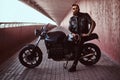 Stylish fashionable biker dressed in a black leather jacket with sunglasses holds a helmet sitting on his custom-made Royalty Free Stock Photo