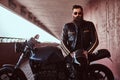 Stylish fashionable biker dressed in a black leather jacket with sunglasses holds a helmet sitting on his custom-made Royalty Free Stock Photo