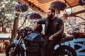 Stylish fashionable biker in sunglasses dressed in a black leather jacket, sitting on his custom-made retro motorcycle Royalty Free Stock Photo