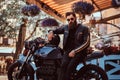 Stylish fashionable biker in sunglasses dressed in a black leather jacket, sitting on his custom-made retro motorcycle Royalty Free Stock Photo