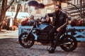 Stylish fashionable biker in sunglasses dressed in a black leather jacket, sitting on his custom-made retro motorcycle Royalty Free Stock Photo