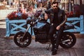 Stylish fashionable biker in sunglasses dressed in a black leather jacket, sitting on his custom-made retro motorcycle Royalty Free Stock Photo