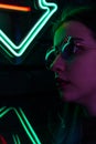 Stylish fashionable teenage girl in glasses with reflection looks up on the street with neon illumination of the city Royalty Free Stock Photo