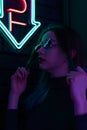 Stylish fashionable teenage girl in glasses with reflection looks up on the street with neon illumination of the city. Royalty Free Stock Photo