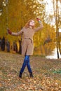 Stylish woman in beige coat and gloves standing in autumn yellow park.