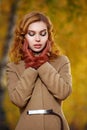 Stylish woman in beige coat and gloves standing in autumn yellow park.