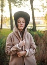 Stylish and fashionable young lady in beige coat and hooded cloak in a park on background of tree, beauty portrait of woman Royalty Free Stock Photo