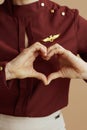 Stylish female air hostess showing heart hands against beige