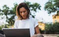 Stylish female entrepreneur working with modern laptop outdoor in summer at city park. Young professional woman looking monitor Royalty Free Stock Photo