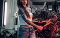 Stylish female model with tattoed body repairs a car engine suspended on a hydraulic hoist in the workshop. Photo with Royalty Free Stock Photo