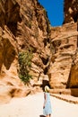 Stylish female tourist in trendy hat and sky-blue dress explore canyon Siq leading to The Treasury, Al Khazneh. Travel and