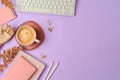 Stylish feminine table with coffee cup, notebook and computer keyboard over purple background. Back to school concept. Top view,