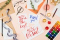 Stylish flatlay with art supplies, envelopes, brushes, watercolors, glasses, pen and a handmade cards