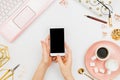 Stylish flatlay frame arrangement with woman`s hands holding white smartphone with black copyspace, pink laptop, coffee, planner Royalty Free Stock Photo